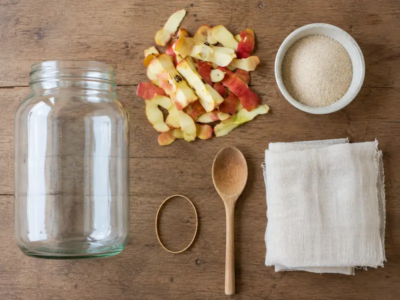 apple cider vinegar from scraps equipment flat lay including glass jar apple peels sugar muslin cloth rubber band and wooden spoon