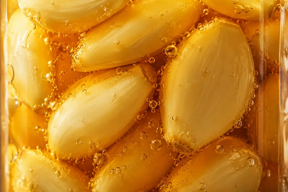 Close-up of garlic cloves fully submerged in honey with fermentation bubbles visible