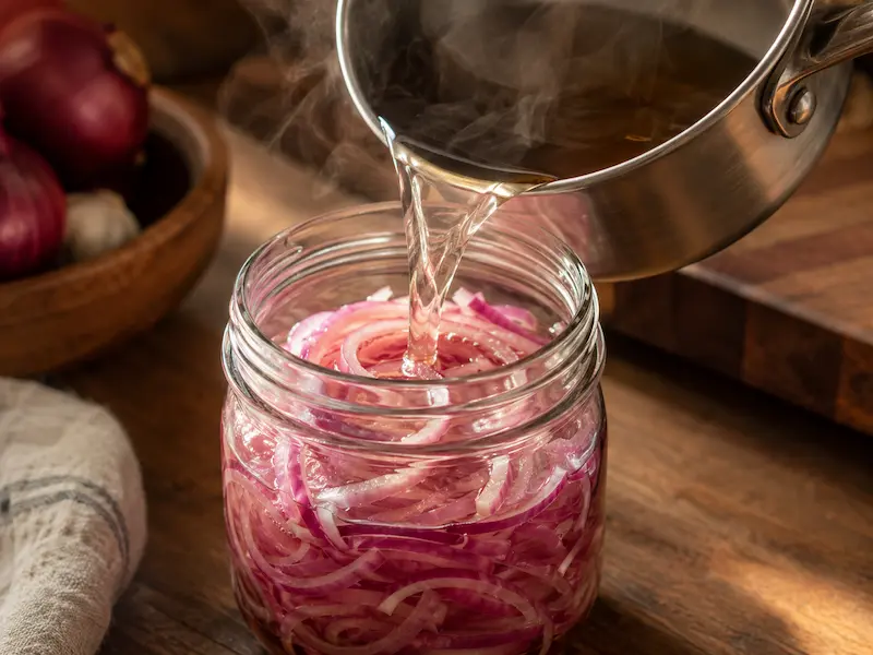 pouring hot brine over sliced red onion in jar