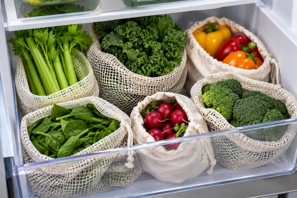 Reusable mesh produce bags filled with vegetables in a refrigerator crisper drawer